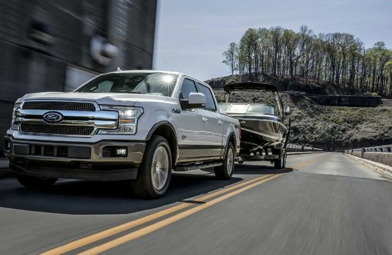 Front view of white 2020 Ford F-150 Lariat towing boat on highway