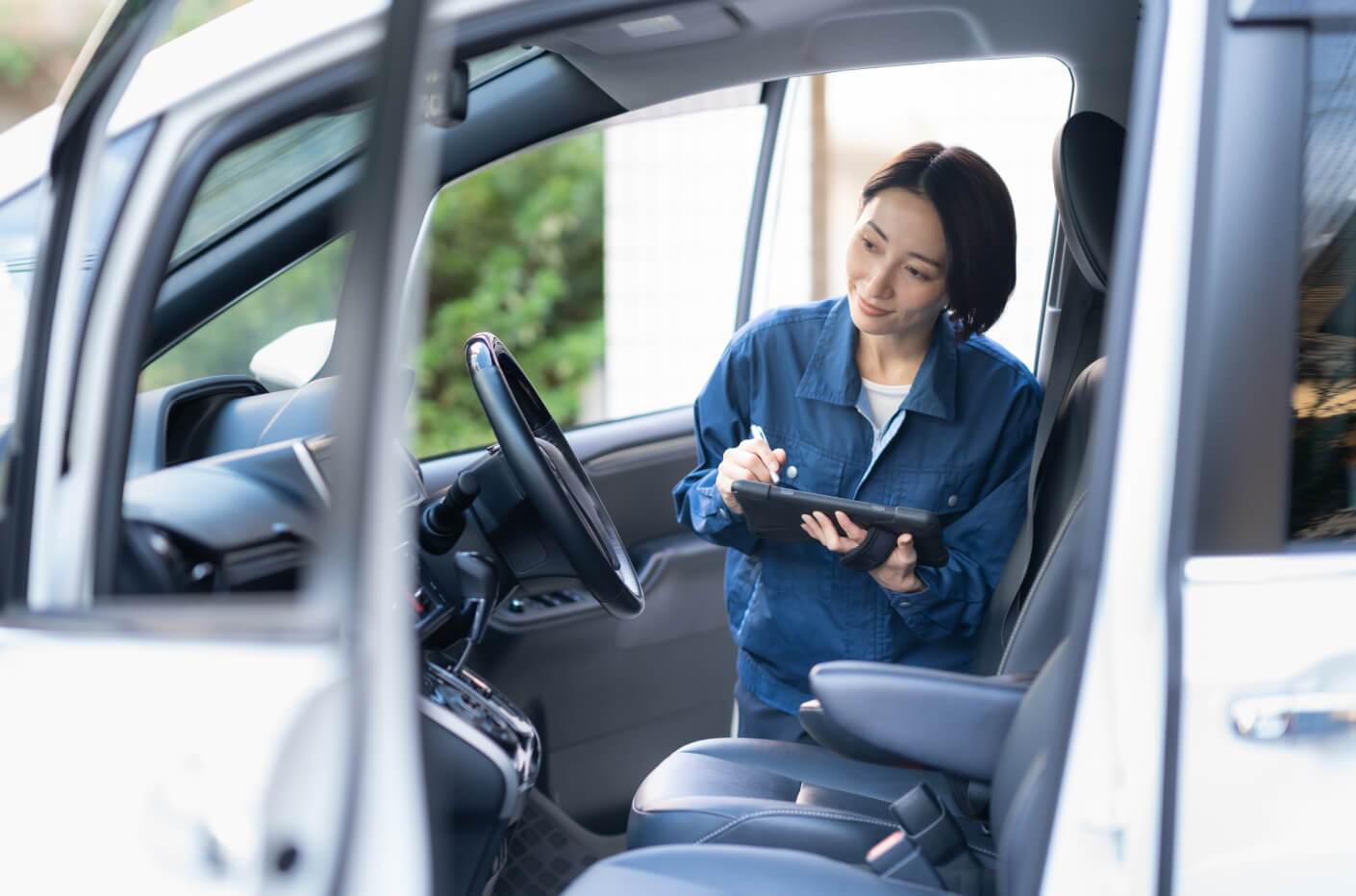 Side view of a female technician inspecting a white car interior with a digital tablet.