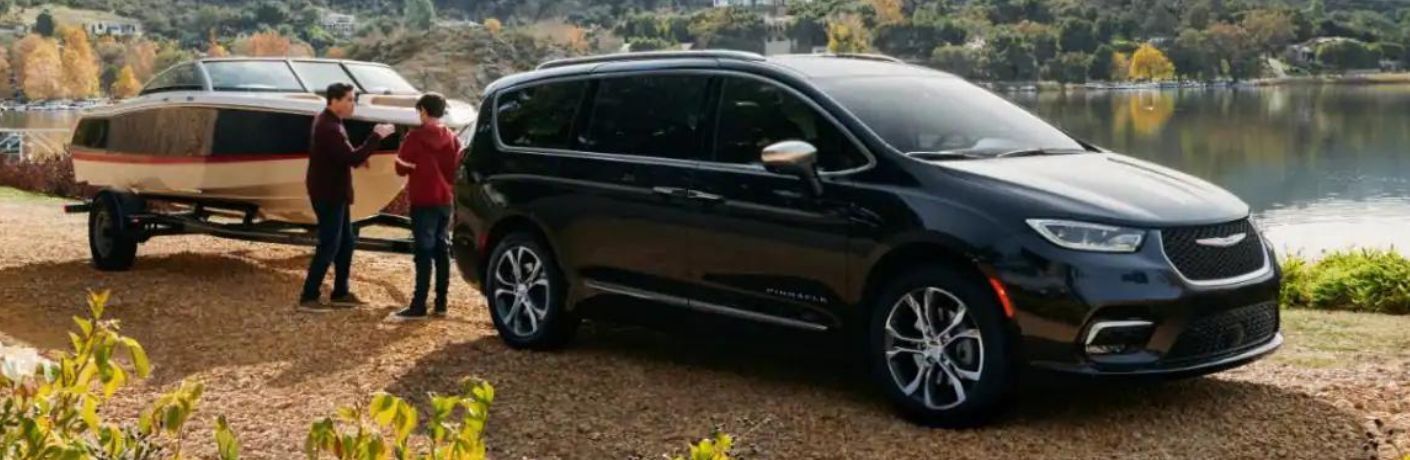 Front three-quarter view of the 2023 Chrysler Pacifica Hybrid Black parked with boat attached