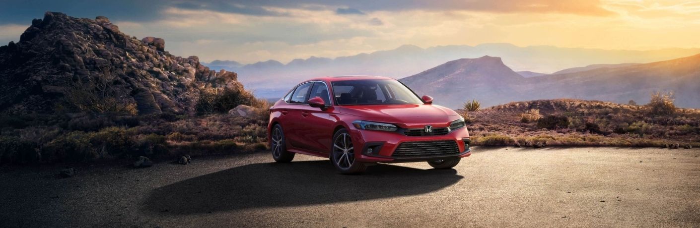 A red-colored 2022 Honda Civic Sedan parked on a clear patch atop a hill
