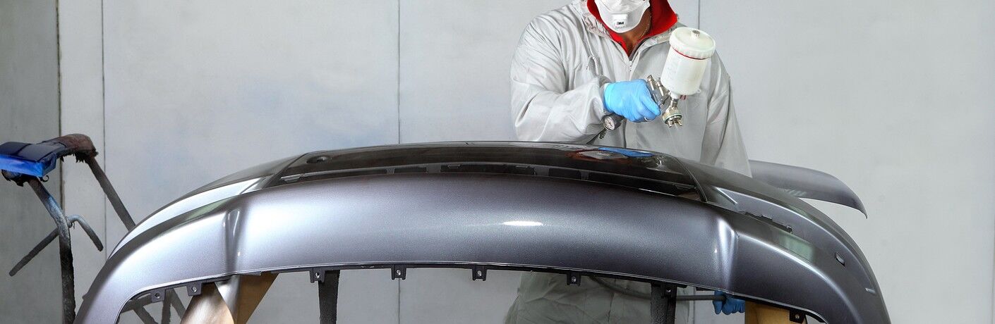 Mechanic painting the bumper of a car grey