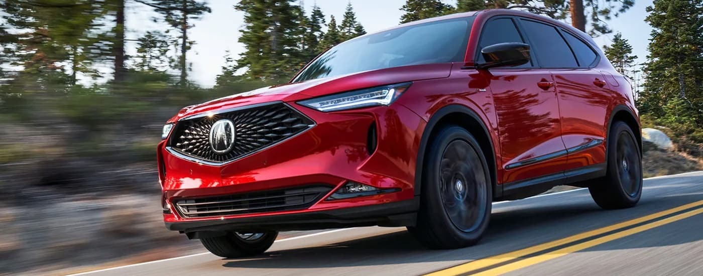 A red 2022 Acura MDX is driving on a tree-lined road after leaving a used car dealership near Elizabeth.