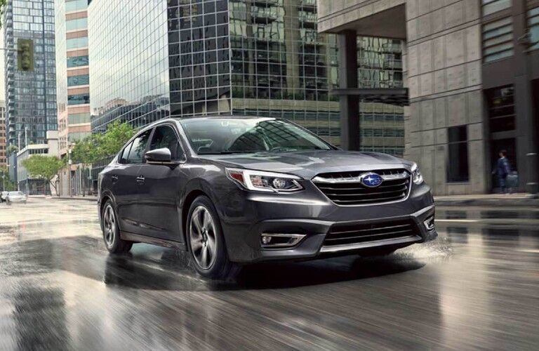 Front passenger angle of a grey 2020 Subaru Legacy driving on a wet road in a city