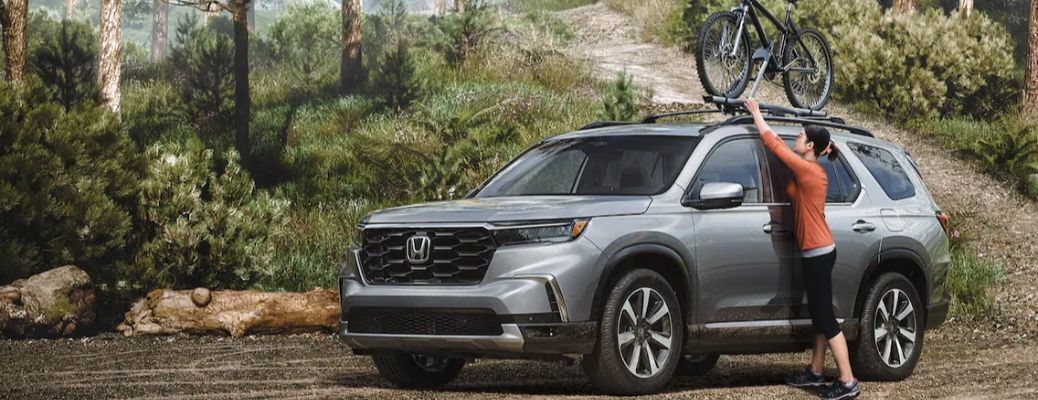 One lady is putting a bicycle on a grey color 2023 Honda Passport.