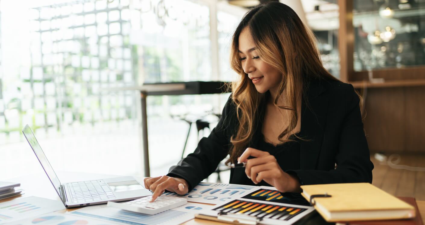 Front view of a woman working with a calculator and financial documents at an office desk.