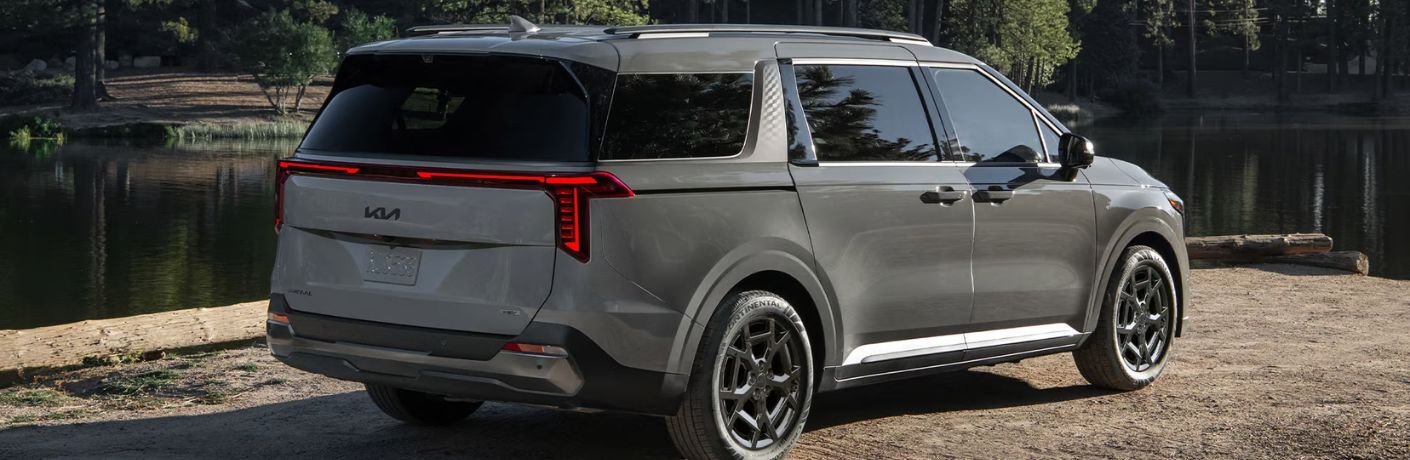 Rear view of the 2025 Kia Carnival MPV Hybrid parked near a lake