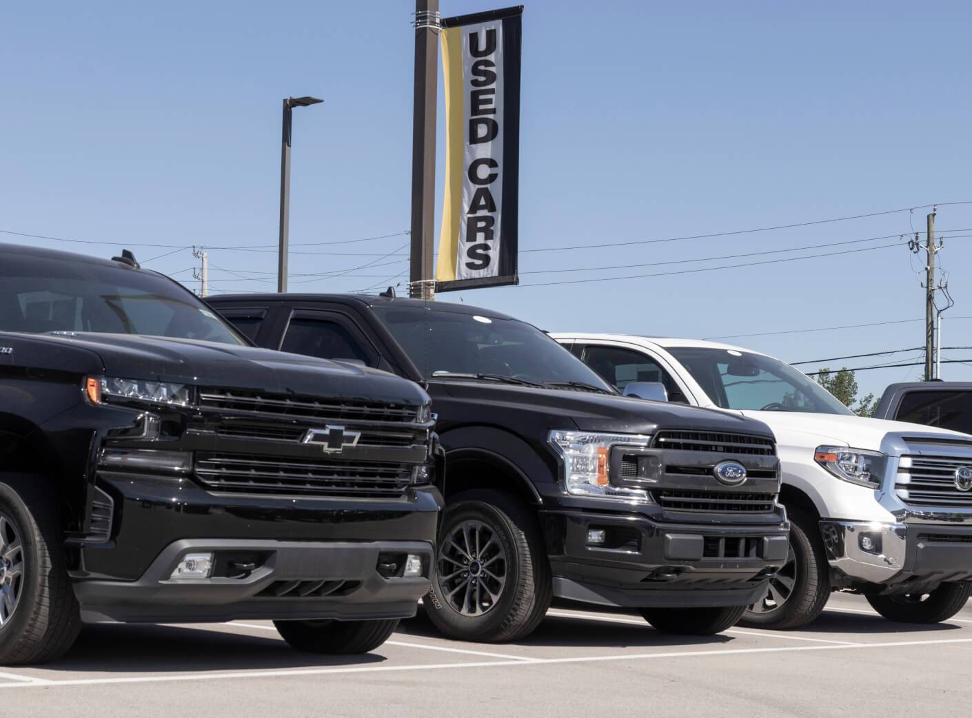 Low-angle front view of black Chevrolet, black Ford, and white Toyota trucks at a used car lot.