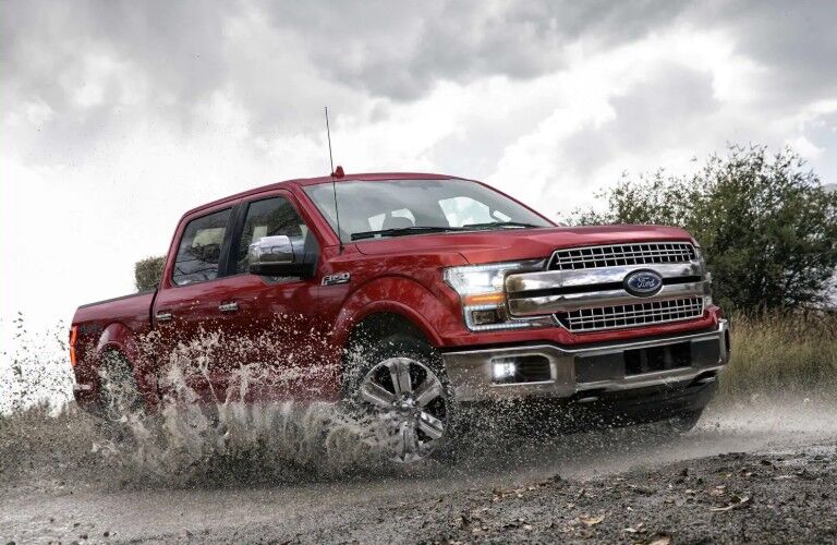 Profile view of red 2019 Ford F-150 Lariat driving through mud
