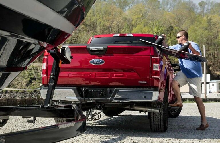 Man loading surfboard in bed area of 2019 Ford F-150 XL