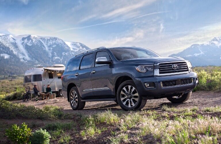 Front passenger angle of a blue 2020 Toyota Sequoia with a family with their trailer in the background