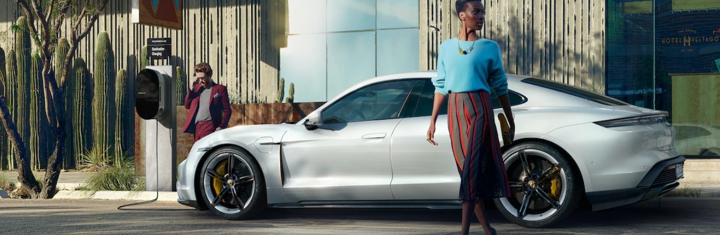 The 2024 Porsche Taycan GTS being charged at the side of the road with a man and woman walking past by 