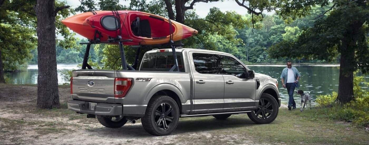 Grey 2023 Ford F-150 with two red kayaks on a bed rack near a river