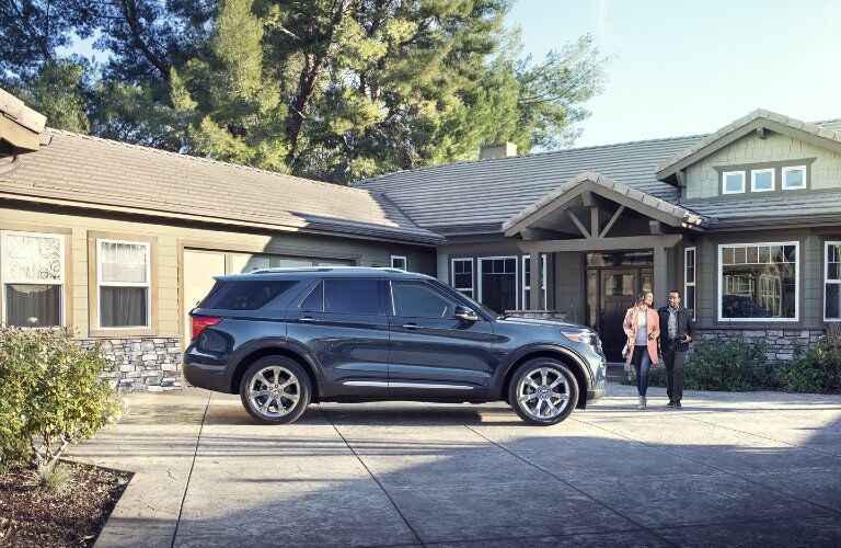 Passenger angle of a blue 2020 Ford Explorer parked by a home with a couple walking towards it