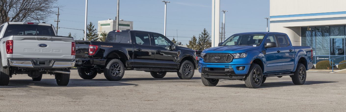 Three Ford trucks parked in front of a used dealership