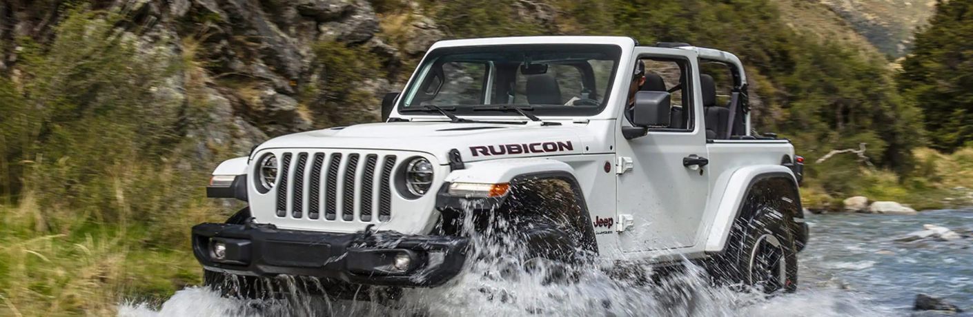 One white color 2022 Jeep Wrangler is running through water.