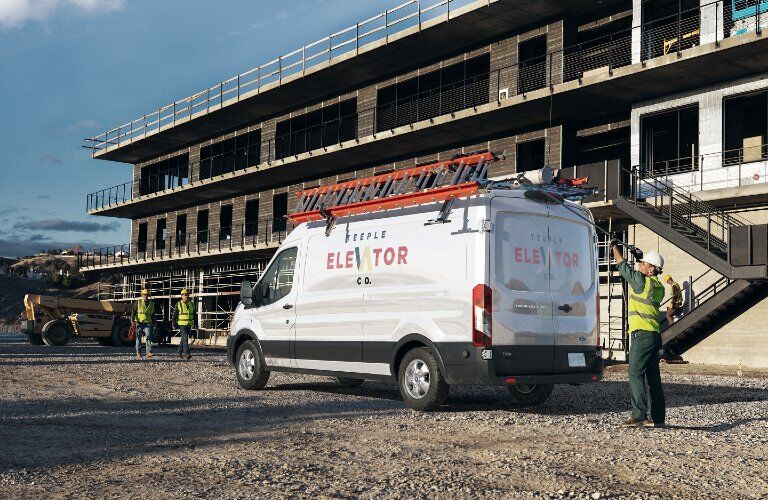 Rear driver angle of a white 2020 Ford Transit with workers working nearby