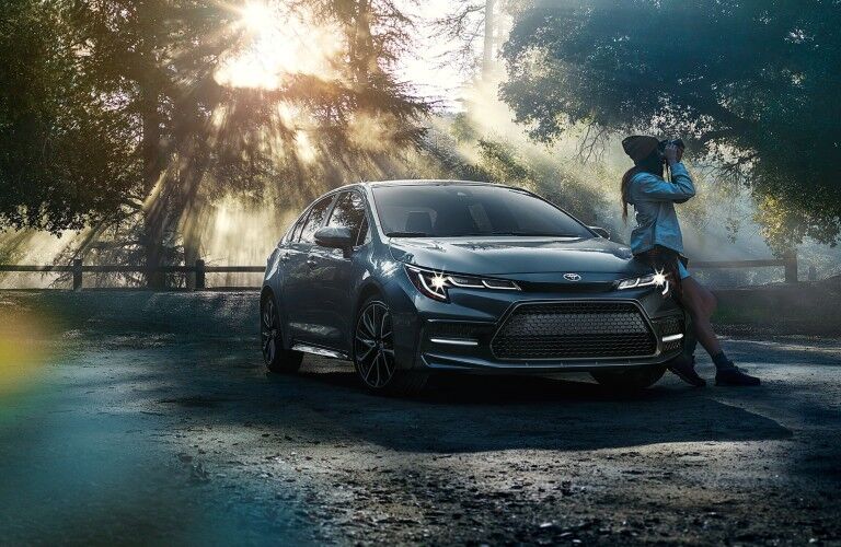 A woman leaning against a parked 2021 Toyota Corolla Sedan