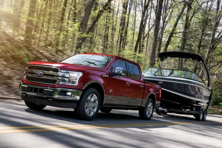 Red 2019 Ford F-150 towing boat down wooded road