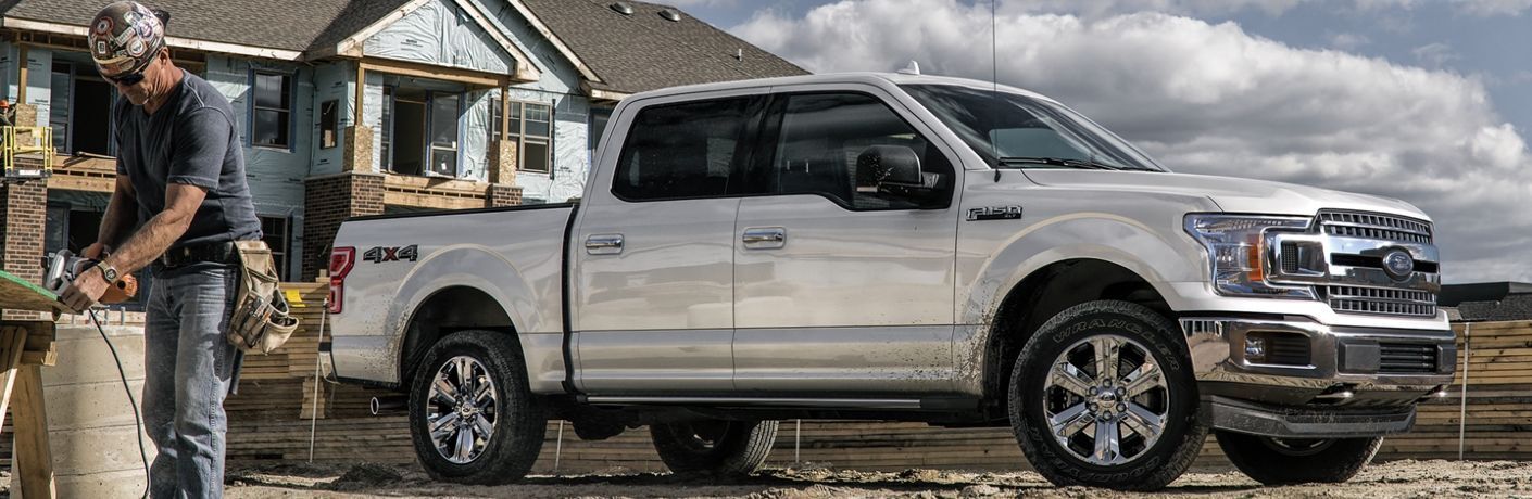 Front passenger angle of a white 2020 Ford F-150 with a man doing construction work nearby
