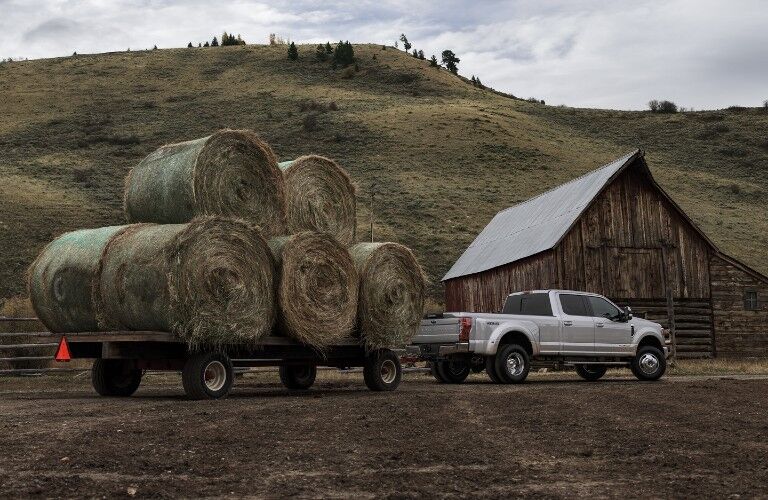Rear passenger angle of a white 2020 Ford Super Duty hitched to a trailer with large rolls of hay loaded on top