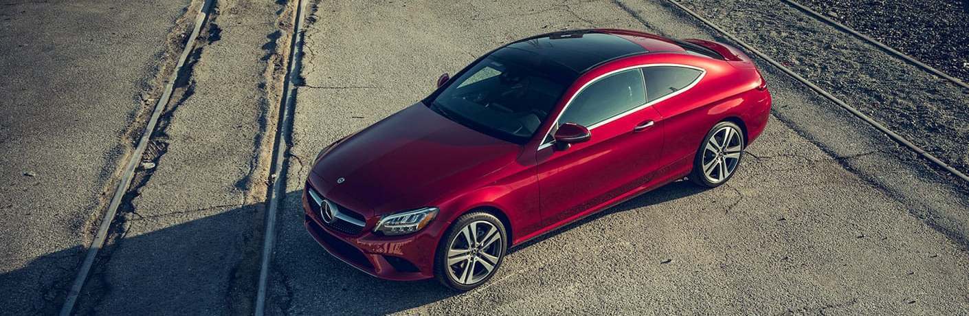 Front driver aerial angle of a red 2020 Mercedes-Benz C-Class Coupe parked by railroad tracks