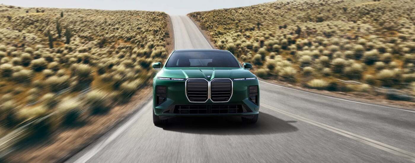 Front view of a green 2026 BMW 7 Series driving down a road.
