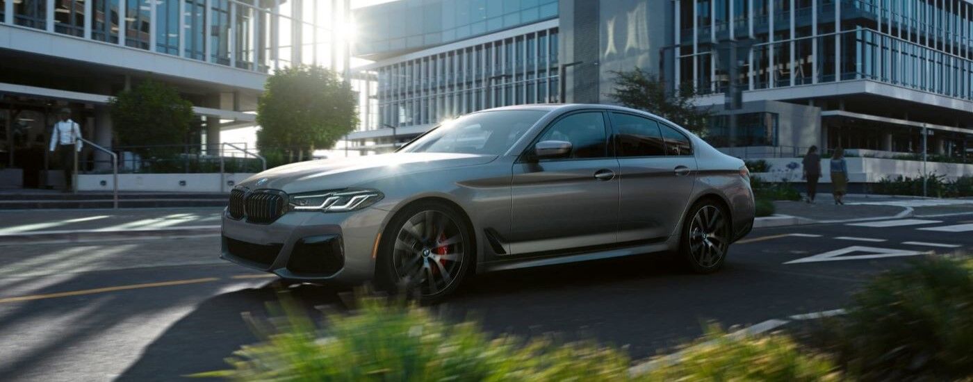 Grey 2023 BMW 5 Series driving down a city street.