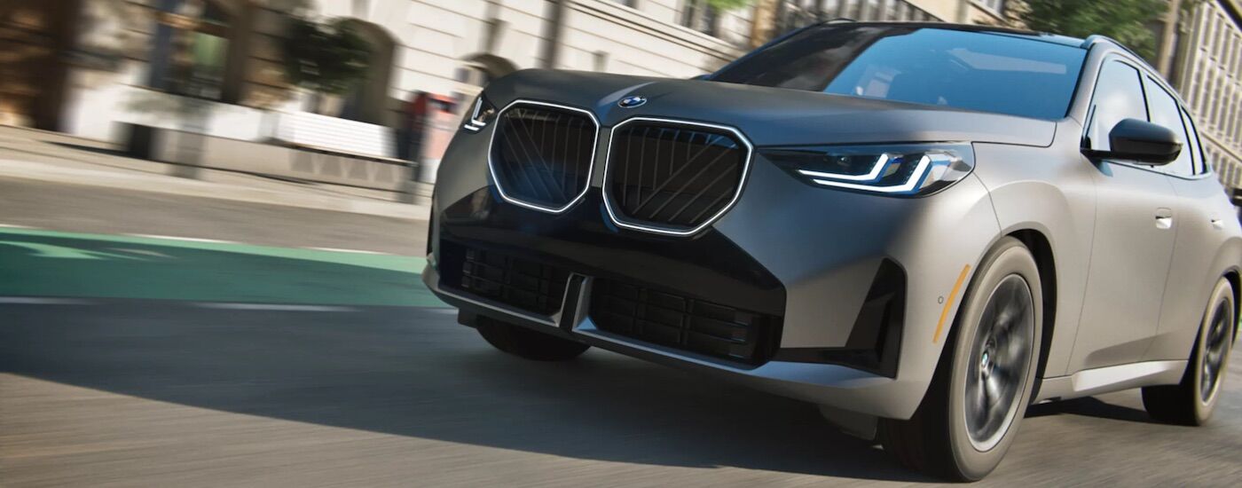 Grey 2026 BMW X3 driving down a city street.