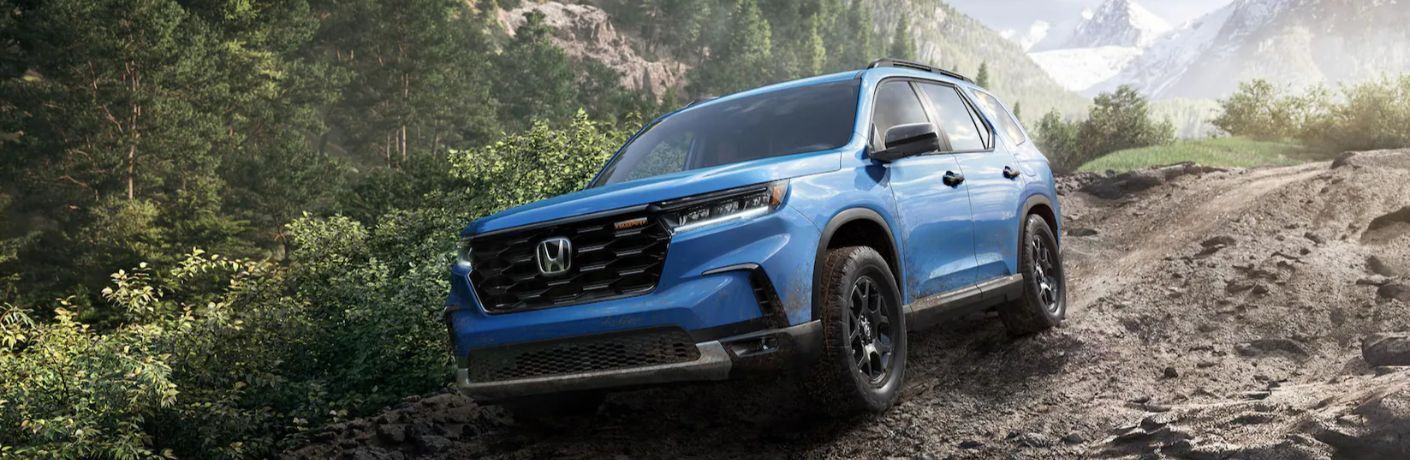 One blue color 2023 Honda Pilot is running on a muddy road.