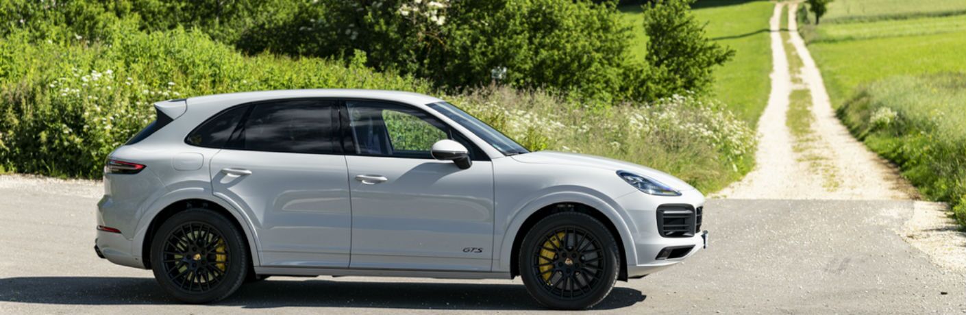 white 2021 Porsche Cayenne passenger side driving on country road past long gravel road