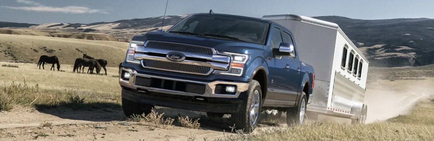 Blue 2019 Ford F-150 King Ranch towing trailer through field