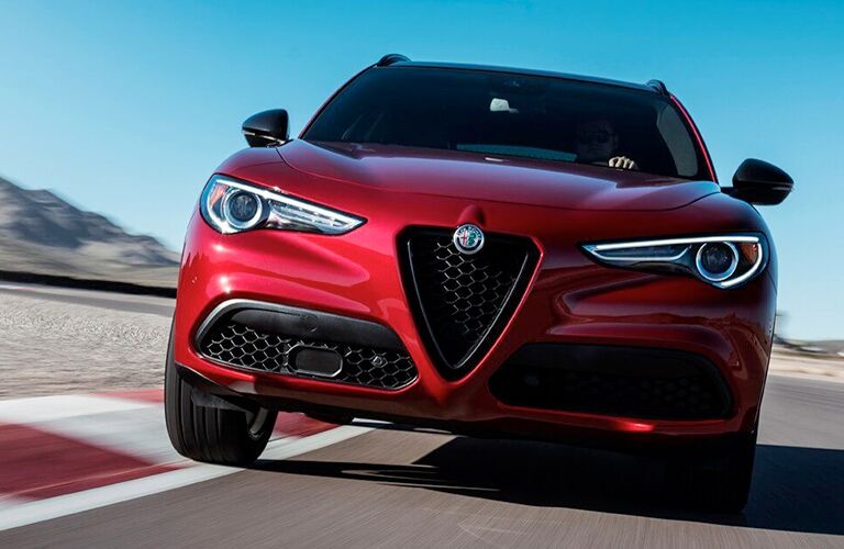 2019 Alfa Romeo Stelvio exterior front shot closeup of headlights and signature grille with Alfa Romeo badge driving around a race track in the wilderness