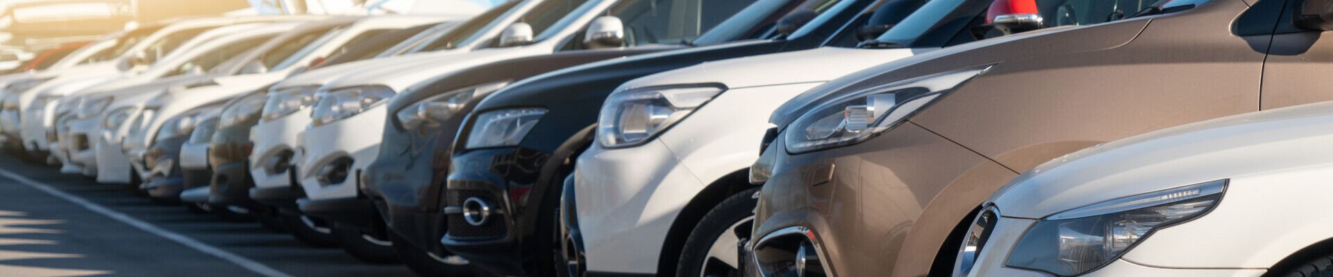 Close-up front three-quarter view of parked cars lined up in a dealership lot.