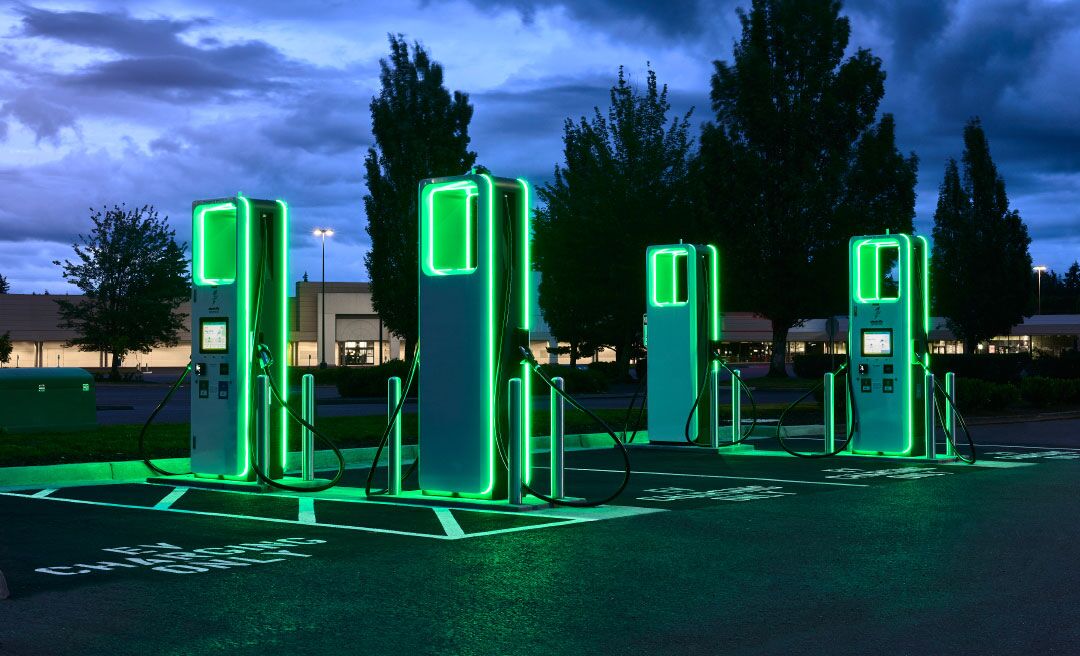 Four electric vehicle charging stations illuminated in green shown in a parking lot at night