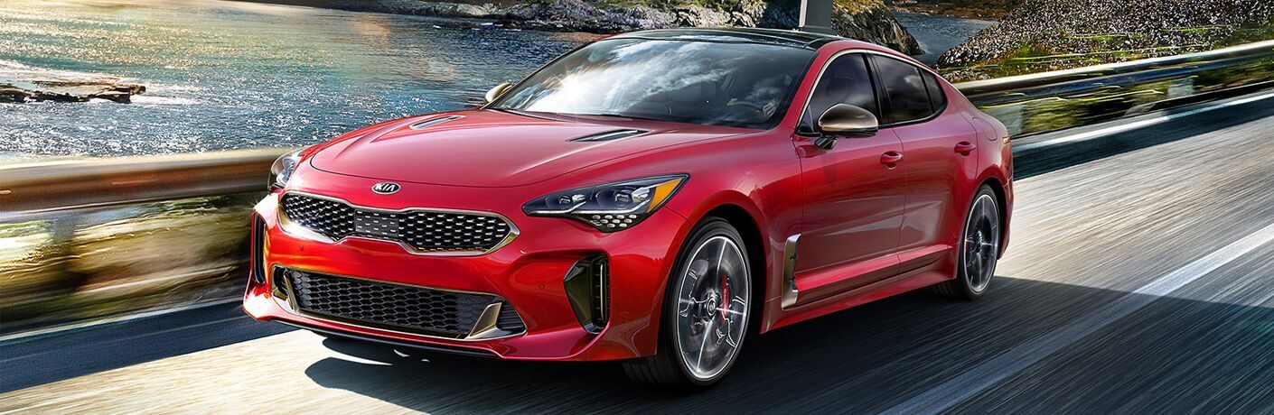 red kia stinger driving by lake