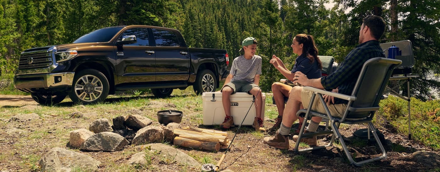 A family is sitting at a campsite next to a brown 2021 Toyota Tundra.