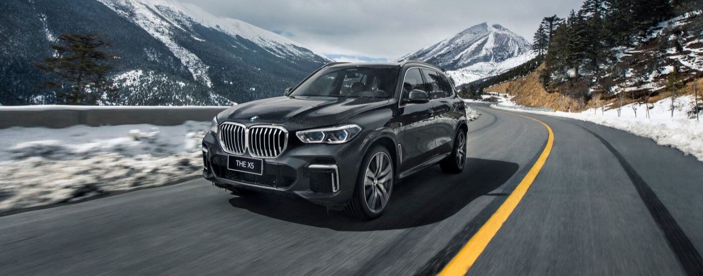 Black 2023 BMW X5 driving around a bend.