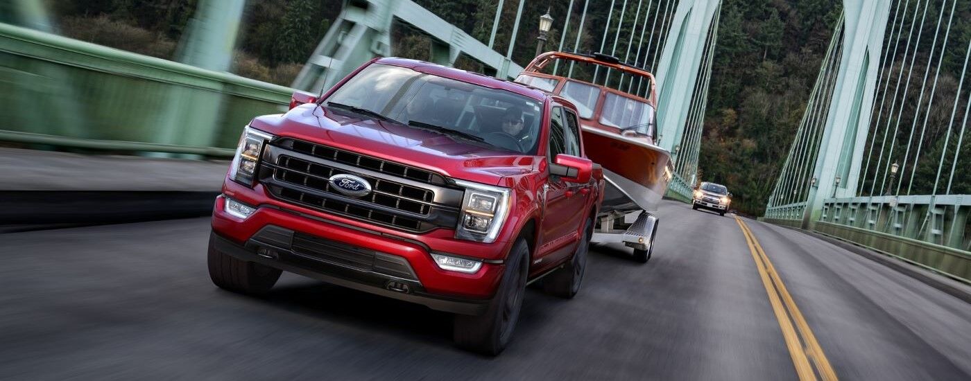 Red 2021 Ford F-150 towing a boat over a green bridge
