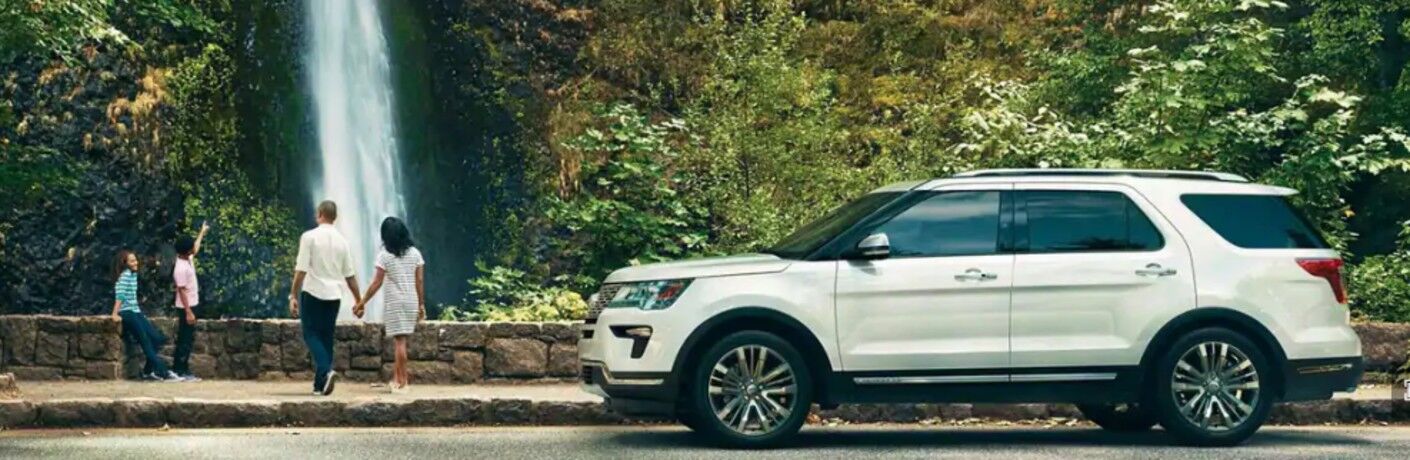 Profile view of white 2019 Ford Explorer Platinum parked in front of waterfall