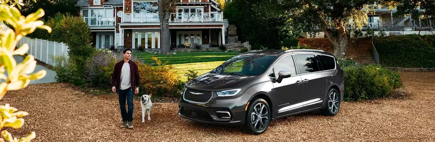 front quarter view of the 2024 Chrysler Pacifica with a man and dog walking from its side and a house in the background