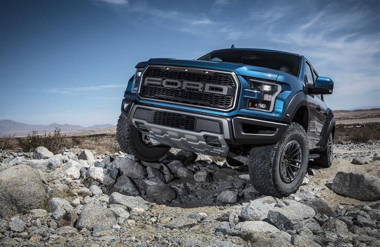 Front view of blue 2019 Ford F-150 Raptor driving on rocky terrain