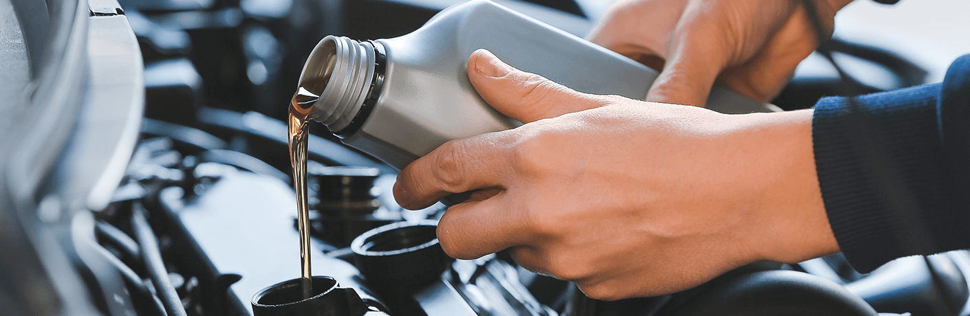 two hands pouring oil into a vehicle engine