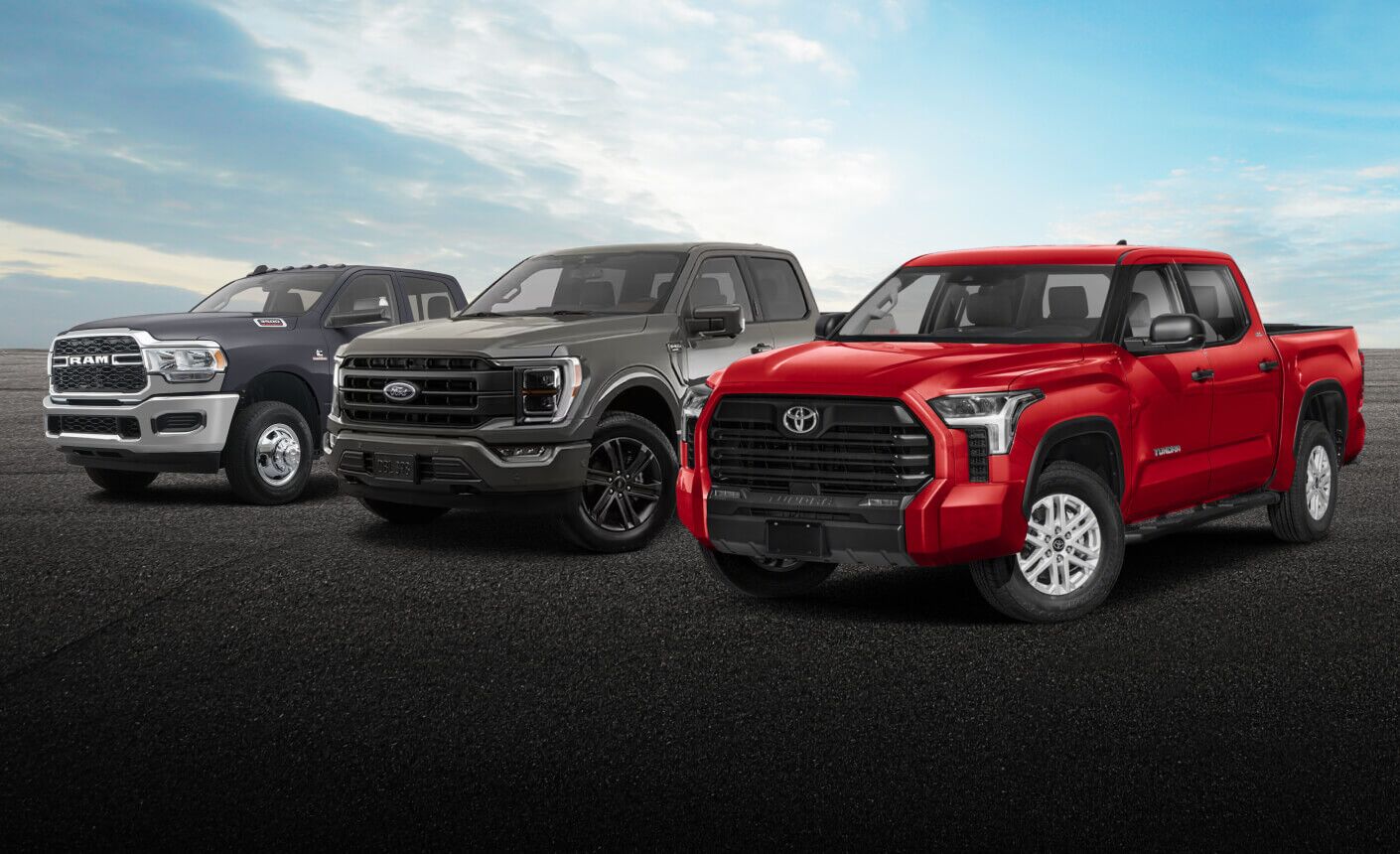 A blue RAM 3500, dark gray Ford F-150 and red Toyota Tundra parked in a lot under a cloudy blue sky.
