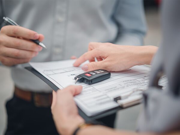 Dealership employee handing a clipboard to the customer with keys on it