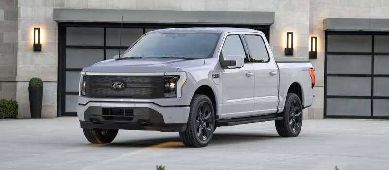 A front 3/4 view of the Ford F-150 Lightning Flash in the driveway of a luxury home