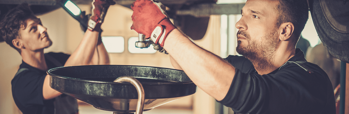 Two technicians performing an oil change on a car