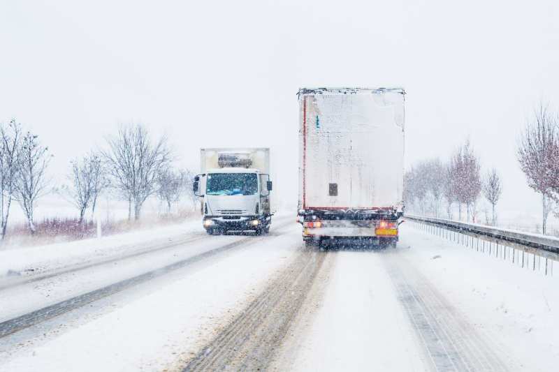 Two winterized heavy trucks passing each other on a snowy road.
