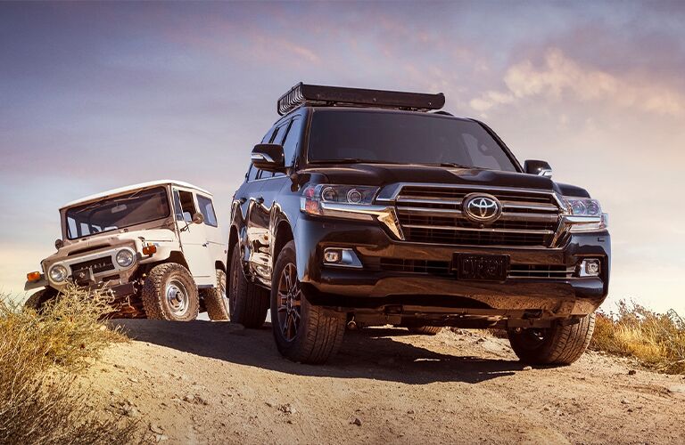 2021 Toyota Land Cruiser black in front of a classic Land Cruiser