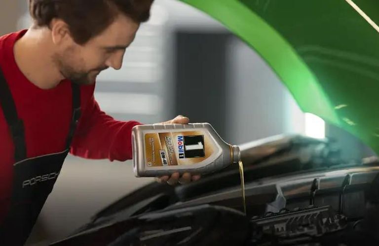 Porsche mechanic pouring oil in a car engine