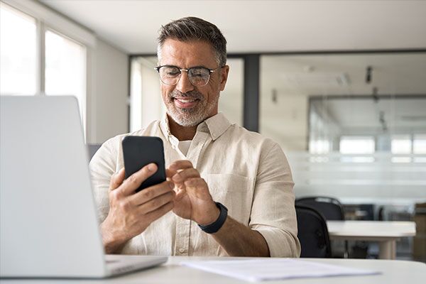 Person sitting in front of laptop while looking at his phone